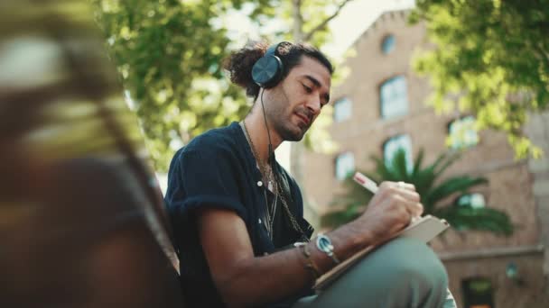 Mladý Italský Chlap Culíkem Strništěm Sedí Sluchátky Lavičce Poslouchá Hudbu — Stock video
