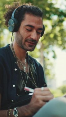At kuyruklu ve sakallı genç bir İtalyan sokak bankında oturmuş müzik dinliyor ve şehir planındaki kağıt üzerine kalemle eskizler çiziyor.