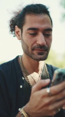 At kuyruklu ve sakallı çekici İtalyan adam eski binaların arkasındaki bankta otururken cep telefonu kullanıyor. Tarz sahibi adam bilgilere bakar, akıllı telefondan fotoğraf çeker.