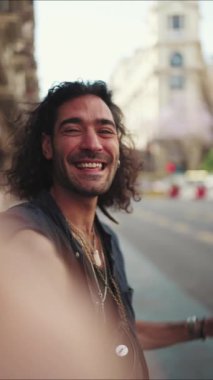 Uzun kıvırcık saçlı ve sakallı genç bir İtalyan sokakta dururken cep telefonundan selfie çekiyor. Akıllı telefonunun kamerasına gülümseyen şık bir adam.