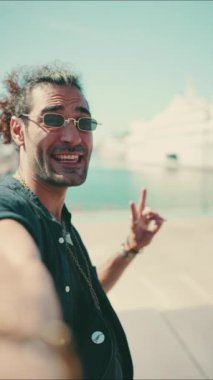 Uzun kıvırcık saçlı ve sakallı genç bir İtalyan cep telefonundan selfie çekiyor. Güneş gözlüklü şık adam akıllı telefonunun kamerasına gülümsüyor.