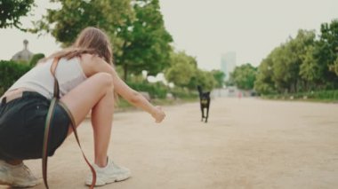 Dişinde top olan mutlu siyah köpek kıza doğru koşuyor. Köpek oyunları yazın dışarıda topun peşinden koşar. Kız parkta evcil hayvanıyla oynuyor.
