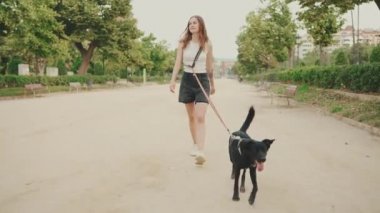 Gülümseyen kız köpekle parkta yürüyor.
