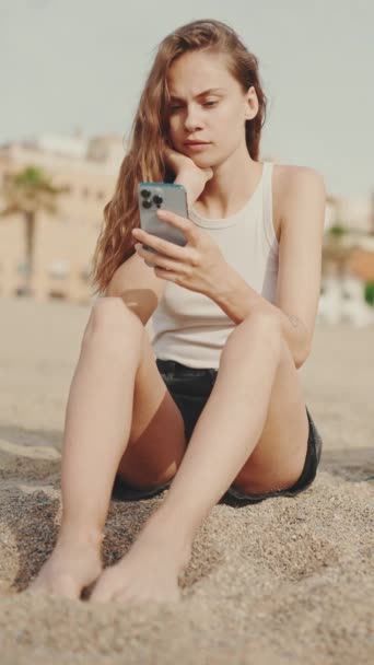 Видео Милая Девушка Мобильным Телефоном Руках Сидит Песке Пляже Современном — стоковое видео