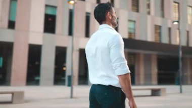 Sakallı, beyaz gömlekli, olgun bir iş adamı modern şehrin sokaklarında duruyor. Başarılı adam rahatlar, hayattan zevk alır. Kamera hareket ediyor