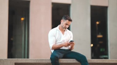 Beyaz gömlek giyen, sakallı, olgun bir iş adamı şehrin finans bölgesinde bankta oturuyor. Başarılı adam akıllı telefondan bilgi aktarıyor.