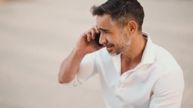 Yakın plan, sakallı, olgun iş adamı cep telefonu kullanıyor şehrin finans bölgesinde bankta oturuyor. Akıllı telefondan konuşan başarılı bir adam. Kamera hareket ediyor