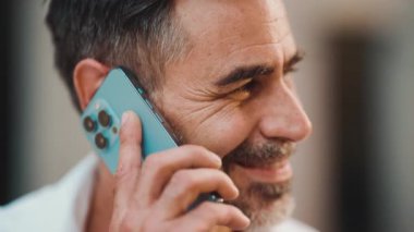 Yakın plan, sakallı, olgun iş adamı cep telefonu kullanıyor şehrin finans bölgesinde bankta oturuyor. Akıllı telefondan konuşan başarılı bir adam. Kamera hareket ediyor