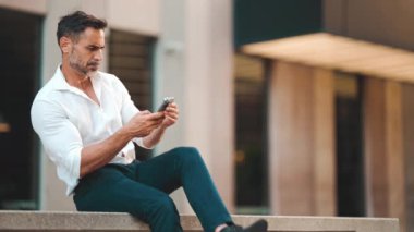 Beyaz gömlek giyen, sakallı, olgun bir iş adamı şehrin finans bölgesinde bankta oturuyor. Başarılı adam akıllı telefondan bilgi aktarıyor.
