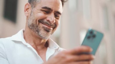 Sakallı, olgun bir iş adamı cep telefonu kullanıyor şehrin finans bölgesinde bankta oturuyor. Başarılı bir adam akıllı telefon ve gülücüklerle bilgi toplar.