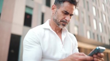 Sakallı, olgun bir iş adamı şehrin finans bölgesinde bankta cep telefonu kullanıyor. Başarılı bir adam akıllı telefondaki bilgilere bakar başını çevirir ve gülümser.
