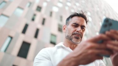 Sakallı, olgun bir iş adamı şehrin finans bölgesinde bankta cep telefonu kullanıyor. Başarılı bir adam akıllı telefon ve gülücüklerle bilgi toplar.