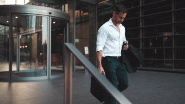 Sakallı, beyaz tişörtlü, olgun bir iş adamı şehrin finans bölgesindeki ofisinden ayrılıyor. Çok çalıştıktan sonra elinde cep telefonu olan başarılı bir adam.