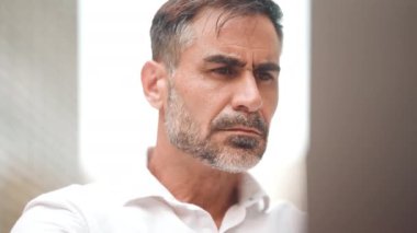 Düz sakallı, olgun bir iş adamı laptopta beyaz gömlek giyiyor bilgisayar açık kafede oturuyor. Doğada açık havada, kafede oturan başarılı bir adam. Mobil ofis serbest.