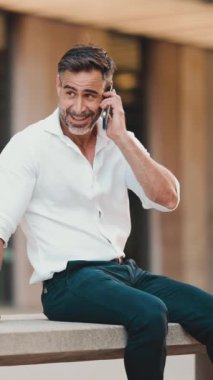 Beyaz gömlek giyen, sakallı, olgun bir iş adamı modern şehrin sokaklarında bankta oturuyor. Başarılı adam dinleniyor.
