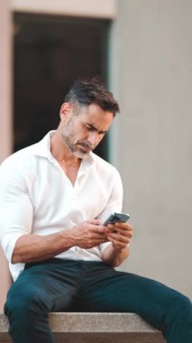 Beyaz gömlek giyen, sakallı, olgun bir iş adamı şehrin finans bölgesinde bankta oturuyor. Başarılı adam akıllı telefondan bilgi aktarıyor.