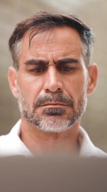 Düz sakallı, olgun bir iş adamı laptopta beyaz gömlek giyiyor bilgisayar açık kafede oturuyor. Doğada açık havada, kafede oturan başarılı bir adam. Mobil ofis serbest.