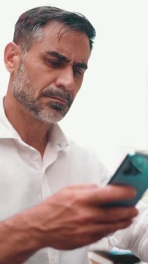 Kafe masasında oturan, kahve içen ve akıllı telefondan yazı yazan düzgün sakallı, olgun bir iş adamı.