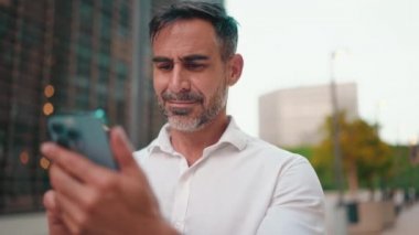 Sakallı, gülümseyen, olgun iş adamı cep telefonu kullanıyor. Başarılı bir adam akıllı telefondan mesaj göndererek bilgileri aktarır.