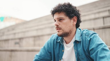 Üzgün adam merdivenlerde oturur ve duygusal düşünür. Kot gömlekli duygusal sakallı genç adamın yakın plan portresi yüksek basamaklarda oturuyor..