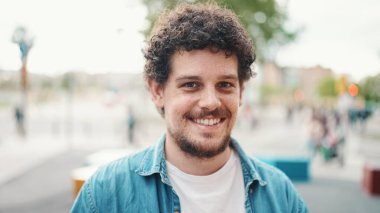  Kot gömlekli genç sakallı adamın yakın plan portresi modern şehir arka planında kameraya poz verip gülümsüyor..