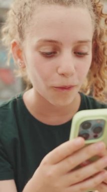 Üç genç kız arkadaş rıhtımda oturmuş videolar izliyorlar, açık havada kentsel arka planda fotoğraflar. kamera hareket ediyor