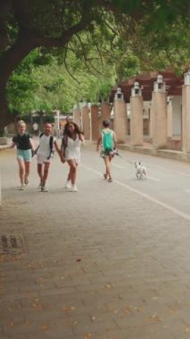 Üç kız arkadaş ergenlik öncesi el ele tutuşup şehrin arka planında hoplayıp zıplıyorlar.