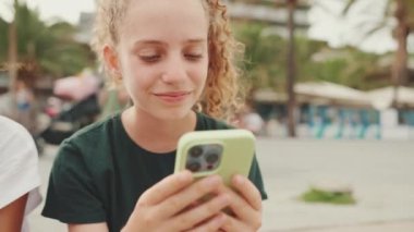 Genç kız rıhtımda otururken cep telefonu kullanıyor. Genç kız akıllı telefondan video görüşmesi yapıyor.