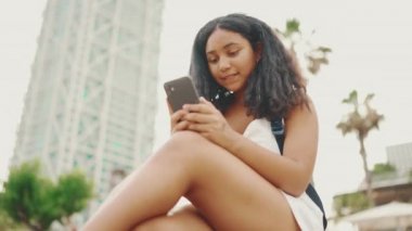 Genç kız rıhtımda otururken cep telefonu kullanıyor. Genç kız akıllı telefondan video görüşmesi yapıyor.