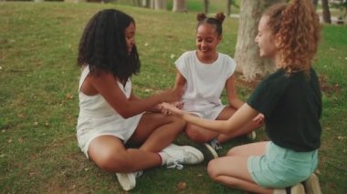 Parktaki çimenlerde oturan, el ele tutuşup el çırpan üç kız arkadaşa gülüyorlar.