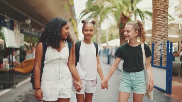 三个十几岁前的女朋友手牵着手站在街上笑着 谈情说爱 3名青少年在户外的城市平民景观背景下 — 图库视频影像