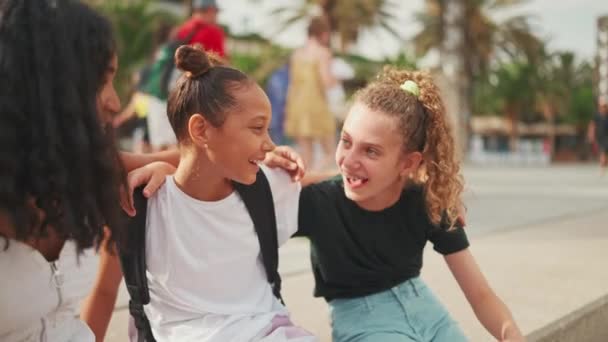 三个十几岁前的女孩朋友坐在海滨笑着 互相拥抱 谈情说爱 城市景观背景下的户外青少年 — 图库视频影像
