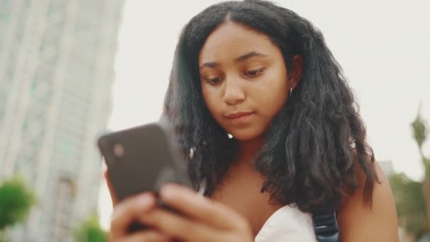 10代前の女の子はウォーターフロントに座っている間に携帯電話を使用します ティーン女の子作るビデオ呼び出しオンスマートフォン — ストック動画