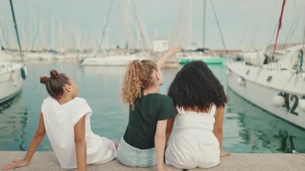 三个未成年的女孩朋友坐在那里 从海滨的背景看游艇和船 背景色 — 图库视频影像