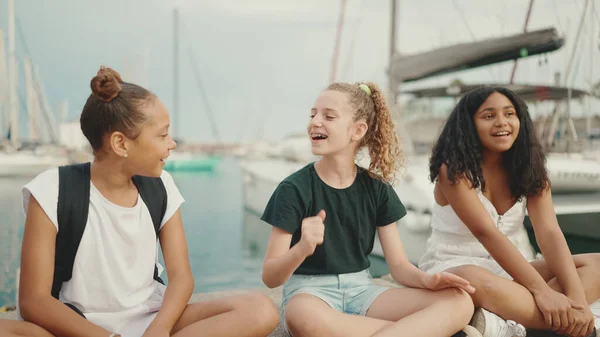 在船舰和游艇的背景下 笑着三个十几岁前的女朋友坐在海滨 青少年在户外海景背景下歌唱和鼓掌 — 图库照片