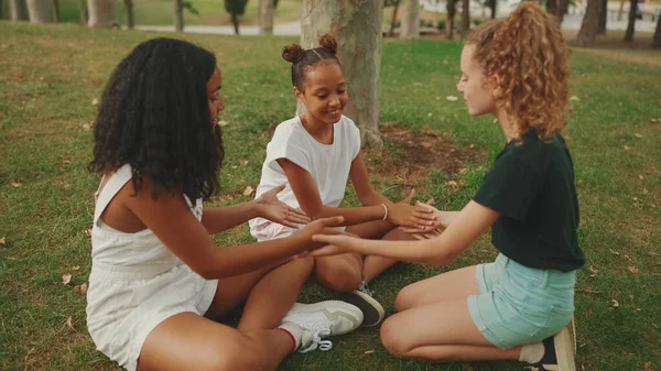 三个青春期前的女朋友坐在公园的草地上 手牵着手 — 图库照片