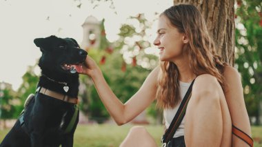 Siyah köpekli tatlı kız çimenlikteki ağacın altında dinleniyor. Mutlu köpek dışarıda yürümekten memnun olur. Açık havada hayvan eğitimi.. 