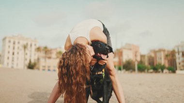 Öğle yemeği vakti. Şirin kız kumsalda evcil hayvanlı sandviçiyle oturuyor. Kız köpeğine sandviçle davranıyor. Modern şehir arka planında sahilde öğle yemeği.