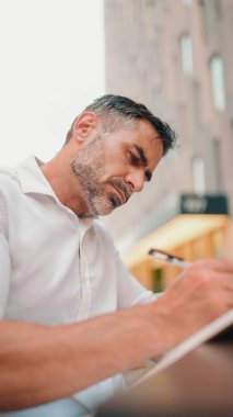 Düzgün sakallı, beyaz gömlekli, kağıt not defterine notlar yazan olgun bir iş adamı masada oturuyor. Randevuları kişisel düzenleyicide günlük görevler yapmak