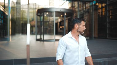 Sakallı, beyaz tişörtlü, olgun bir işadamı şehrin finans bölgesindeki ofisinden ayrılıyor.