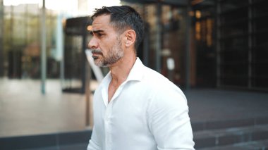 Sakallı, beyaz tişörtlü, olgun bir işadamı şehrin finans bölgesindeki ofisinden ayrılıyor.