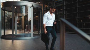 Sakallı, beyaz tişörtlü, olgun bir iş adamı şehrin finans bölgesindeki ofisinden ayrılıyor. Çok çalıştıktan sonra elinde cep telefonu olan başarılı bir adam.