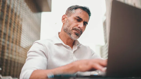 Mature businessman with neat beard wearing white shirt user on laptop pc computer sit at cafe outdoors. Successful man sitting at cafe table outdoors on nature Mobile office freelance