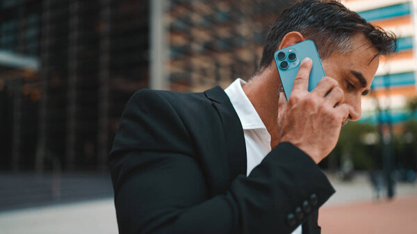 Бизнесмен средних лет с аккуратной бородой в офисной одежде пользуется мобильным телефоном. Успешный человек эмоционально разговаривает на смартфоне. Разочарование, проблемы