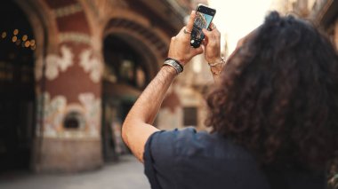 Uzun kıvırcık saçlı ve sakallı çekici İtalyan adam eski bir binanın fotoğrafını çekiyor. Kulağında küpe ve bir sürü zincire bağlı şık bir adam manzara çekiyor..