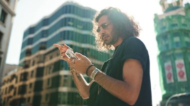 Uzun kıvırcık saçlı ve sakallı çekici İtalyan çocuk cep telefonu kullanıyor. Güneş gözlüklü şık bir adam akıllı telefonundaki haritayla yerini belirliyor.