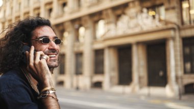 Uzun kıvırcık saçlı ve sakallı çekici İtalyan çocuk cep telefonu kullanıyor. Meşgul caddede akıllı telefondan konuşan şık bir adam.