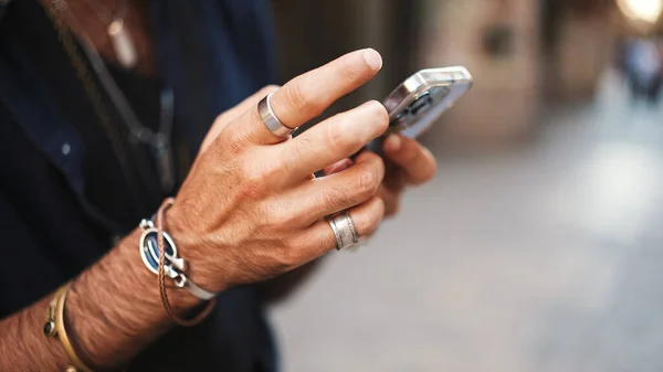 Close-up of male hands in bracelets and rings. Man is using mobile phone. Guy writes message on his smartphone