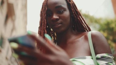 Üstü başı Afrika örgülü muhteşem bir kadın sokakta dikiliyor ve cep telefonu kullanıyor. Şık kız akıllı telefondan mesaj yazıyor.
