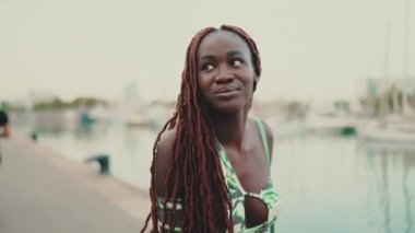 Afrika örgülü güzel bir kadın limanda iskele boyunca yürüyor ve deniz manzarasına bakıyor.